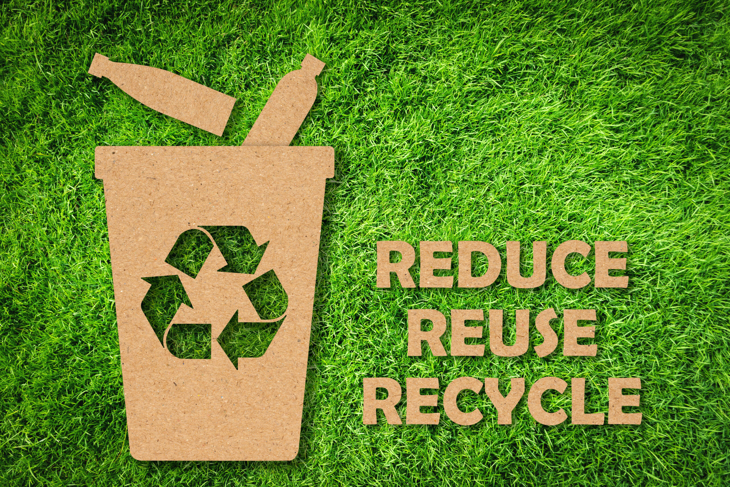 Kraft paper cut of Reuse, Reduce, Recycle symbol and text on green grass background. Environmental conservation concept. Kraft paper cut of Reduce, Reuse, Recycle symbol and text on green grass background. Environmental conservation concept.